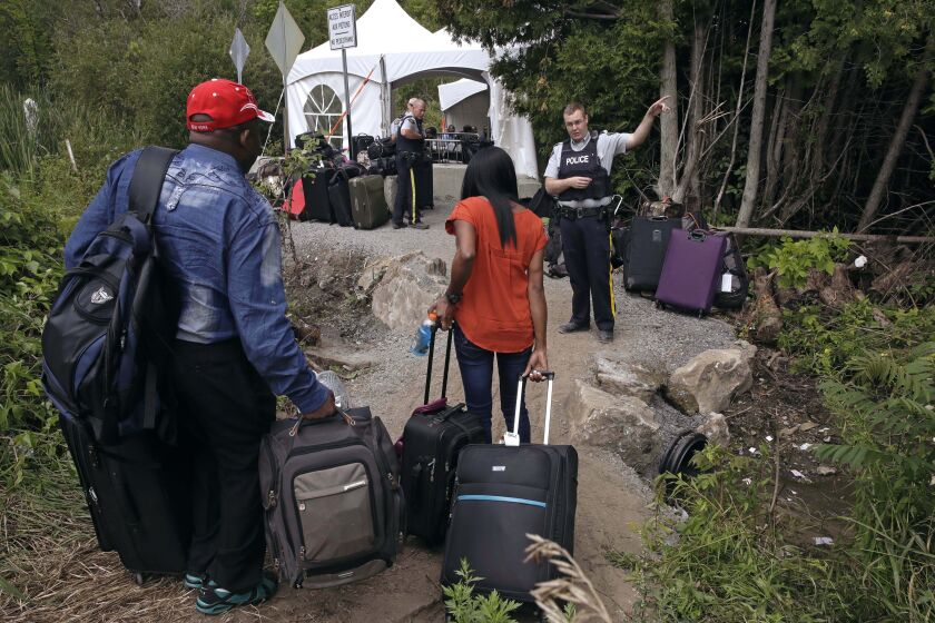 FILE - In this Aug. 7, 2017 file photo, a Royal Canadian Mounted Police officer informs a migrant couple of the location of a legal border station, shortly before they illegally crossed from Champlain, N.Y., to Saint-Bernard-de-Lacolle, Quebec, using Roxham Road. In the first nine months of 2022, the Immigration and Refugee Board of Canada finalized more than 2,700 claims by Mexican asylum seekers. Of those, 1,032 were accepted, 1,256 were rejected; and the remaining 400-plus were either abandoned, withdrawn, or had other outcomes, said Christian Tessier, an IRB spokesperson. (AP Photo/Charles Krupa, File)
