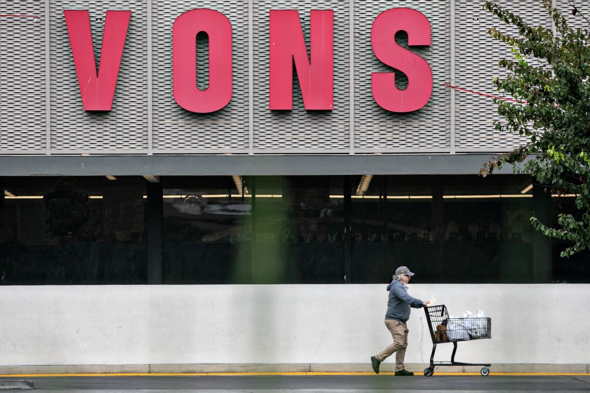 A shopper pushes a cart with bagged groceries outside a Vons
