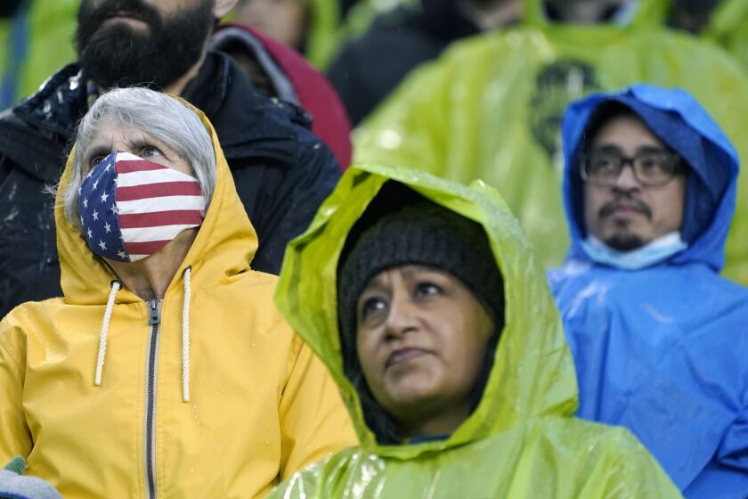 FILE - A person wears a U.S. flag face mask during the national anthem before an MLS soccer match between the Seattle Sounders and Nashville SC, Feb. 27, 2022, in Seattle. Many Americans are significantly relaxing how often they wear masks and take other once-routine precautions against the coronavirus. A new poll from The Associated Press-NORC Center for Public Affairs Research shows fewer than half now say they regularly wear face masks, avoid crowds and skip nonessential travel. Americans are letting their guard down as new COVID-19 infections plummet to their lowest level since July. (AP Photo/Ted S. Warren, File)