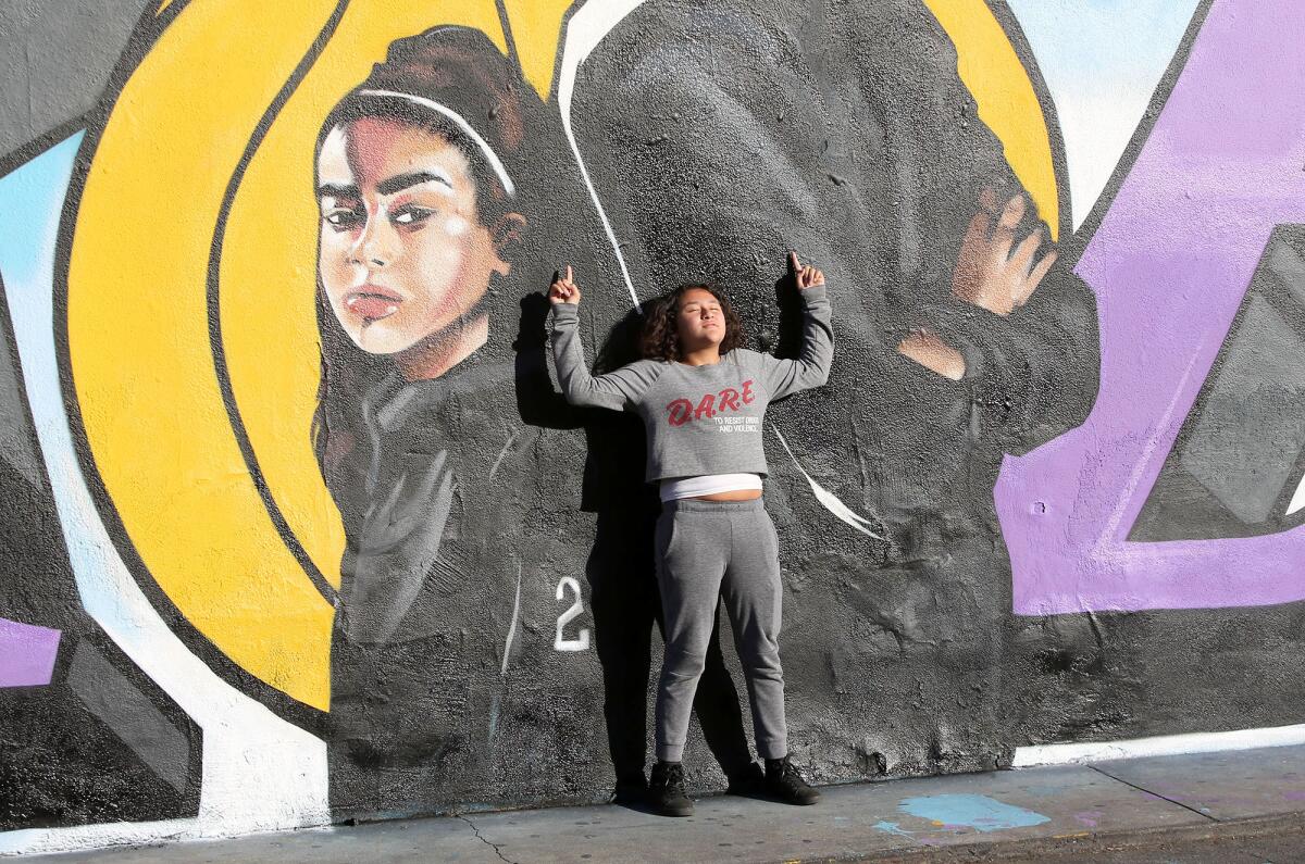A fan poses in front of a mural honoring Kobe and Gianna Bryant on the side of El Toro Bravo market in Costa Mesa.