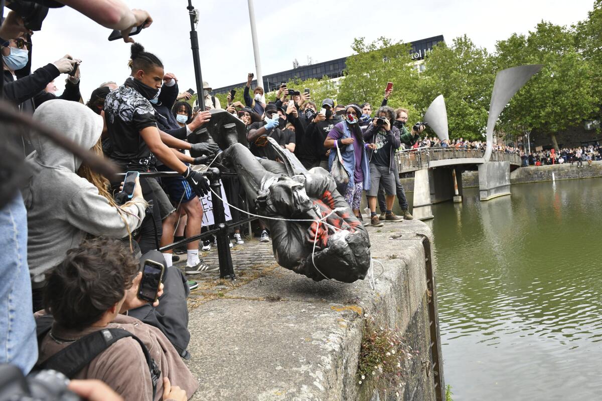 Protesters throw a toppled, tied-up statue of slave trader Edward Colston into the harbor in Bristol, England as crowd cheers