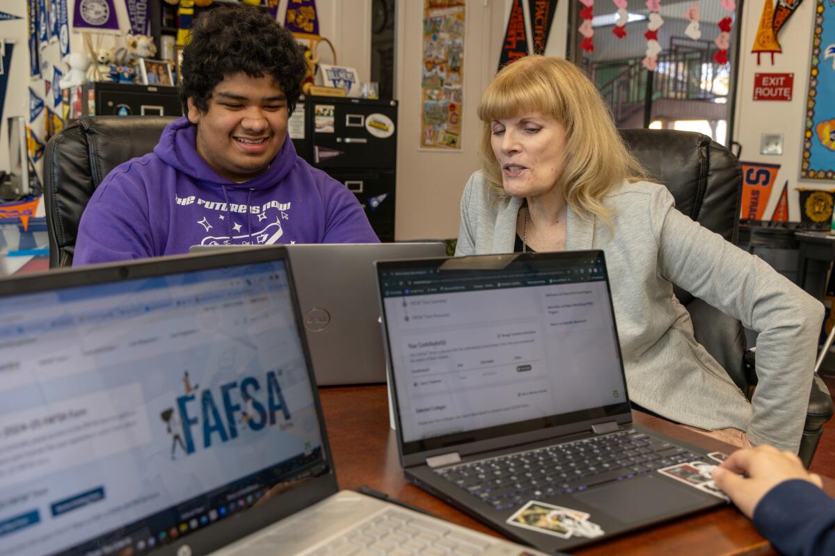 A college counselor and student fill out his FAFSA application on their computers.  