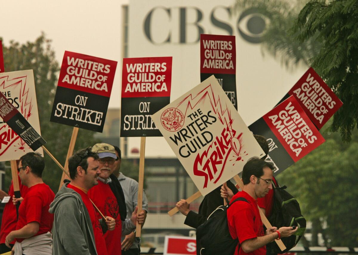 Picketers hold signs that say "Writers Guild of America on Strike" 