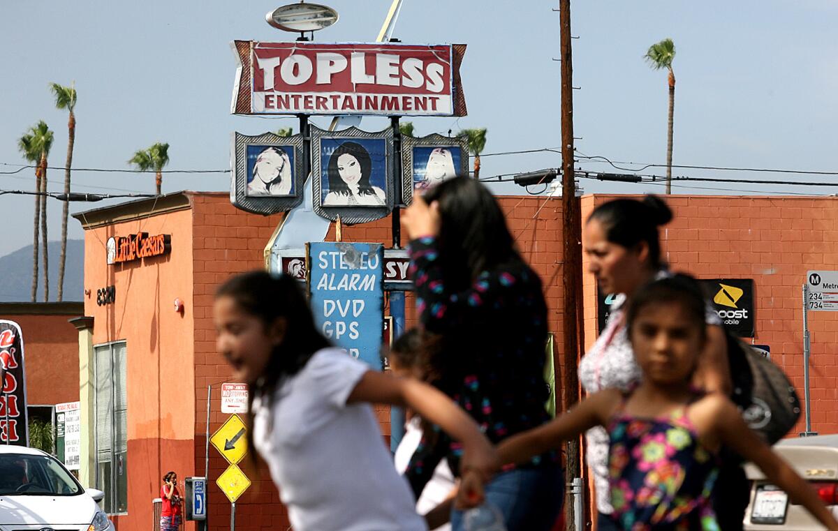 Women and children cross the street at the intersection of Roscoe Boulevard and Sepulveda Boulevard in the Valley with an adult entertainment sign in the background.