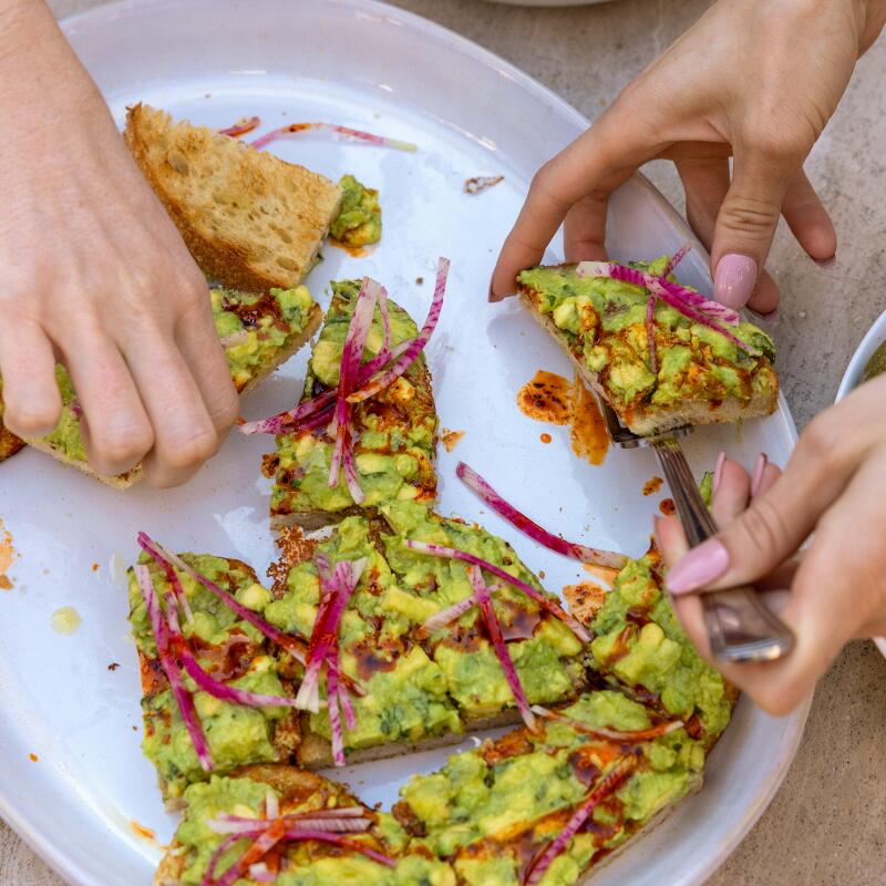 Hands pick up pieces of avocado toast from an oval plate.