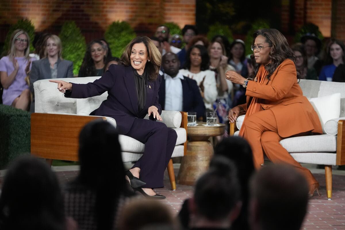 Kamala Harris and Oprah Winfrey sit on a sofa in front of an audience