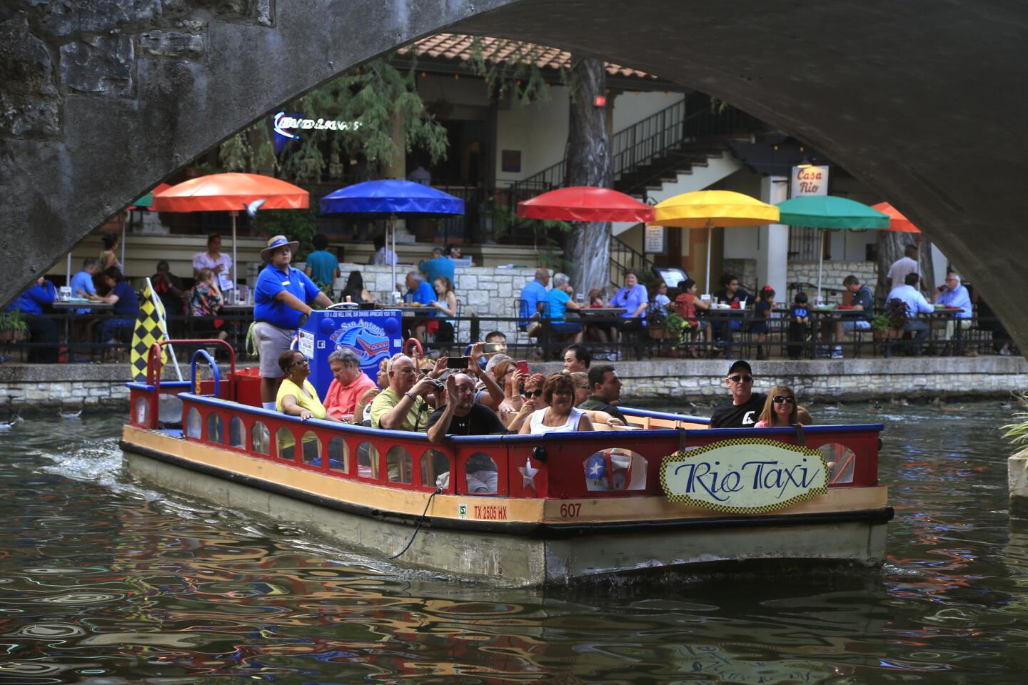 One of the Rio Taxi boats floats past the colorful umbrellas at Casa Rio Restaurant along the riverwalk in San Antonio.