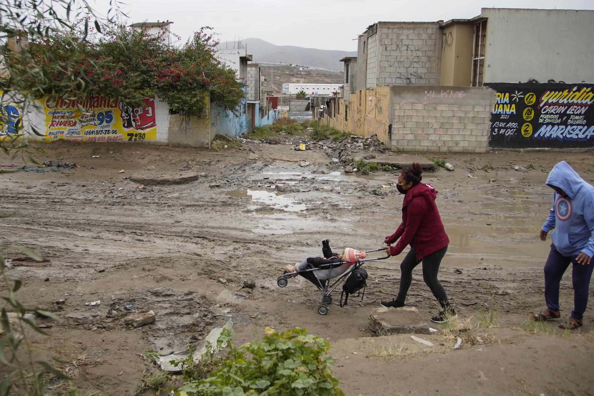 Residents wade through mud near a local swap meet in Colonia La Fuentes in far eastern Tijuana on Wednesday, Dec. 29, 2021. 