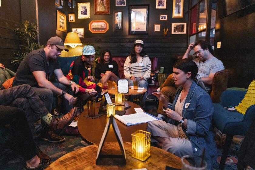 A group of people sitting on couches around a coffee table in a bar and talking together.