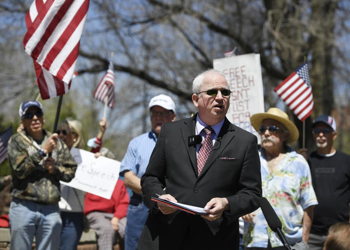 John Eastman, wearing a suit, stands in front of people waving U.S. flags.