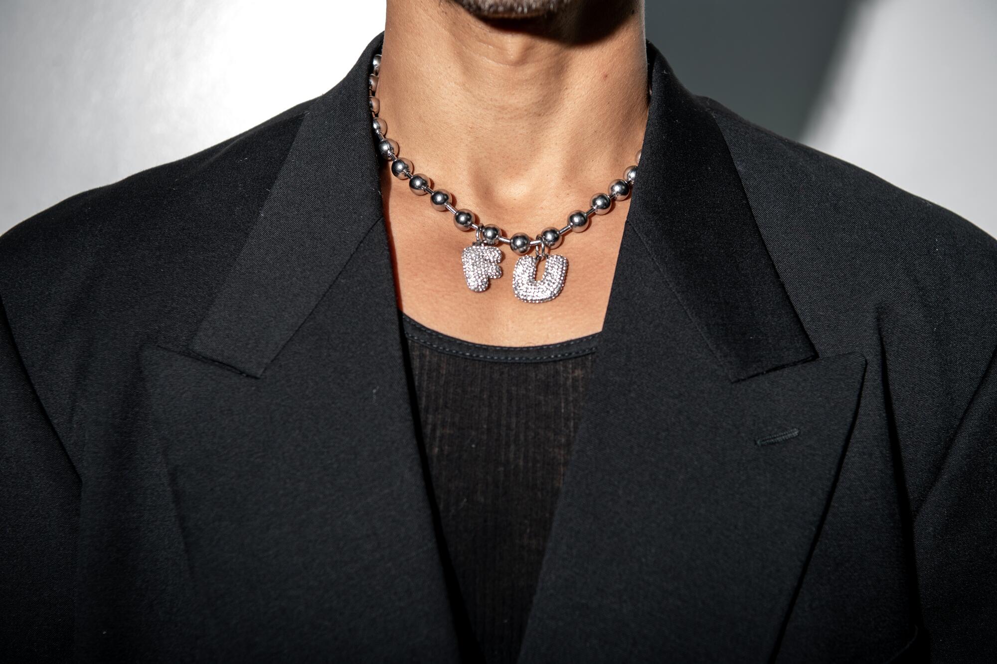 A close-up shot of a man wearing a necklace with the letters "F" and "U."