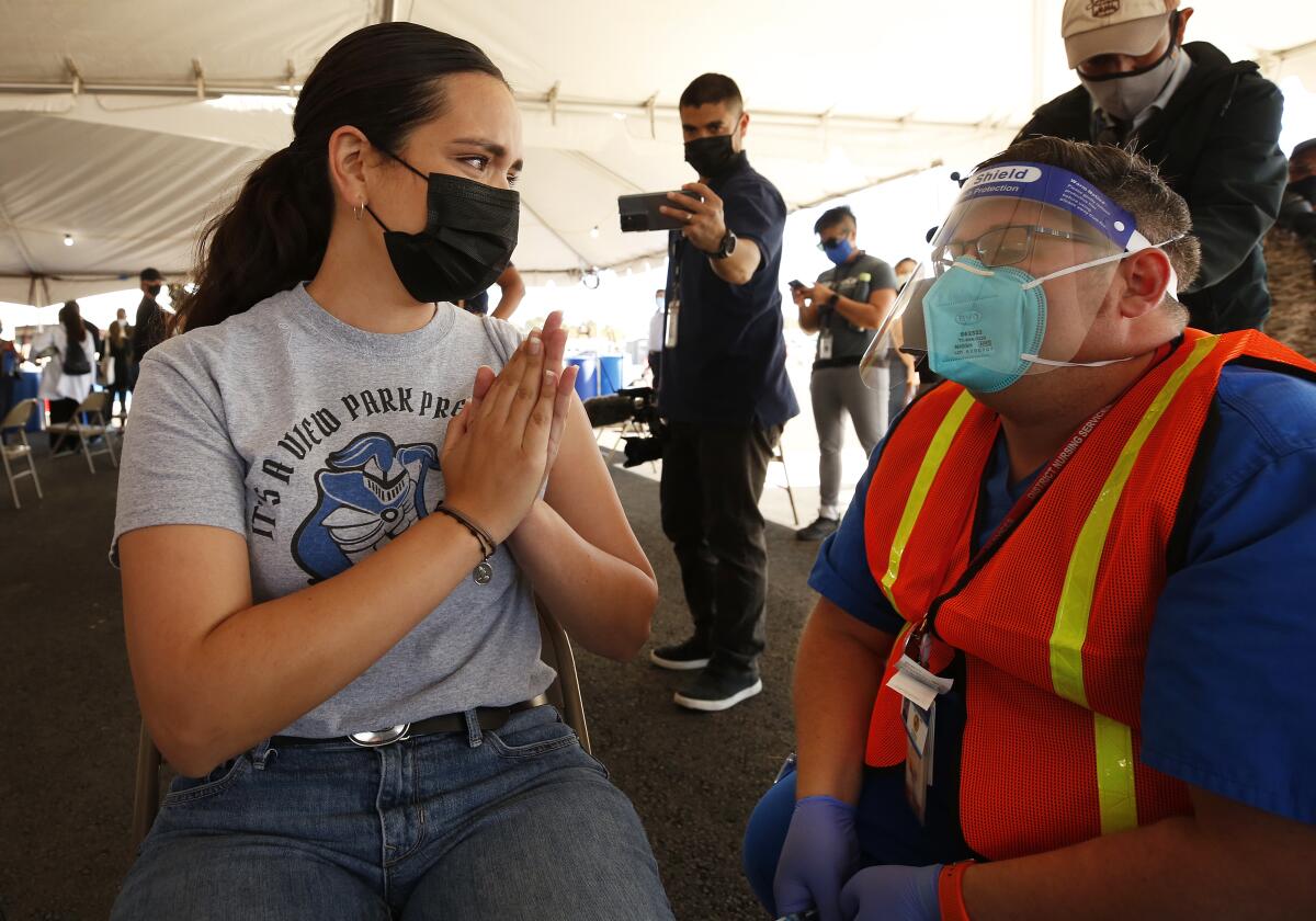 A woman with her hands clasped like they are in prayer looking at a medical worker