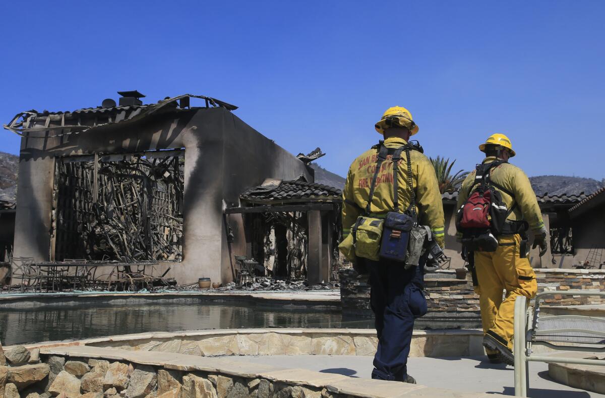 Firefighters walk by a home that was destroyed by fire on a hilltop in Escondido last Friday.