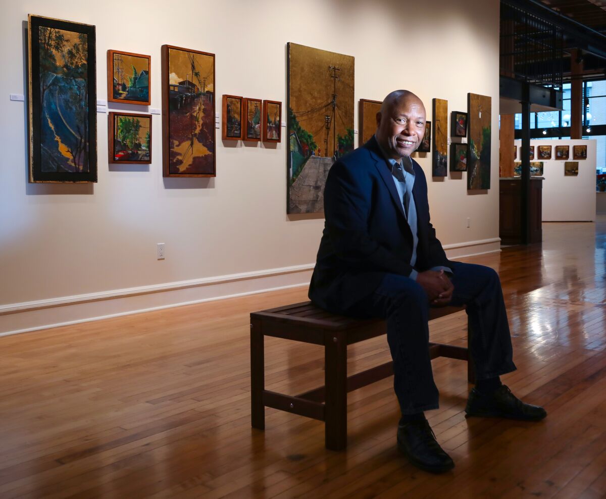 A man sitting on a bench in front of paintings in a gallery