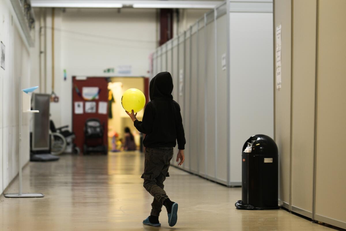 A boy with a ball walks alongside makeshift sleeping units inside the temporary refugee shelter at the former airport Tegel in Berlin, Germany, Wednesday, Nov. 9, 2022. The city of Berlin is turning a former airport into a temporary refugee shelter with 3,600 beds as it is struggling to put up more Ukrainians fleeing Russia's increasingly brutal attacks on their country's energy infrastructure as well as the cold winter months. (AP Photo/Markus Schreiber)