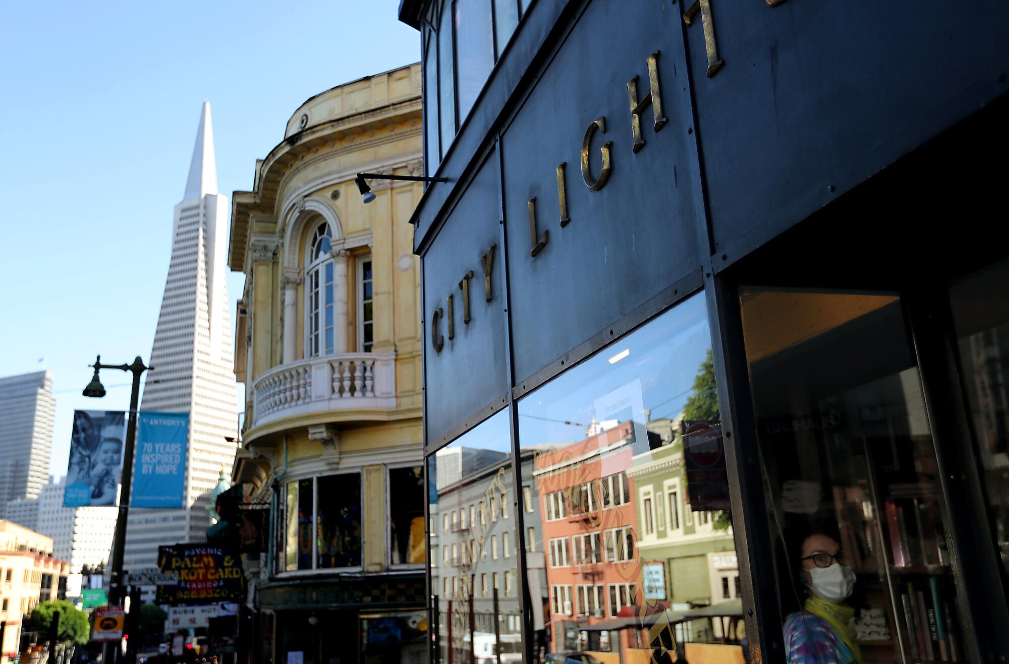 An employee wearing a mask looks out the window of the iconic City Lights bookstore in San Francisco.