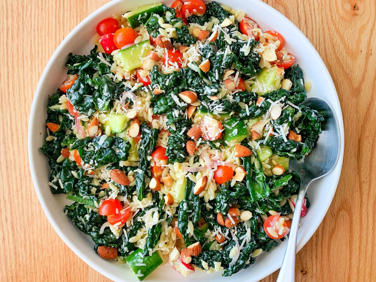 Closeup of a bowl with mixed kale, zucchini, small tomatoes and other ingredients in a dressing.