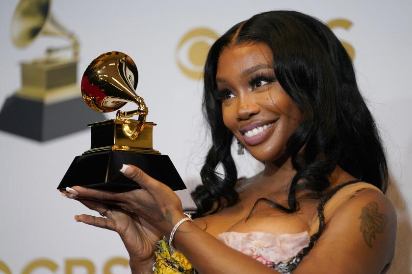 SZA smiles while holding up a golden Grammy trophy.