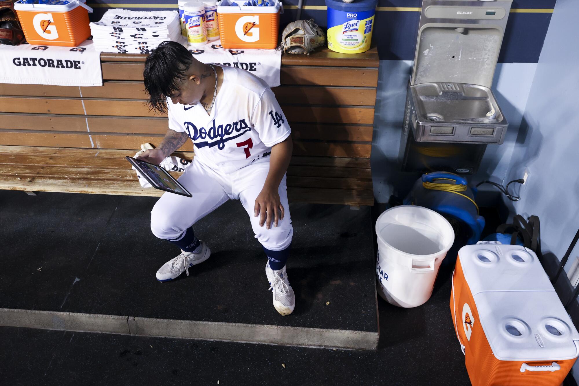 Dodgers starting pitcher Julio Urías sits in the dugout watching plays with a tablet.