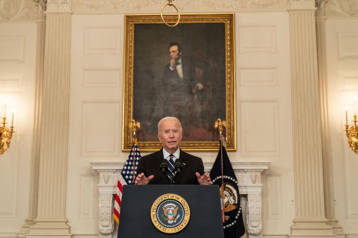  President Biden  speaks at a lectern in front of a painting of Lincoln.