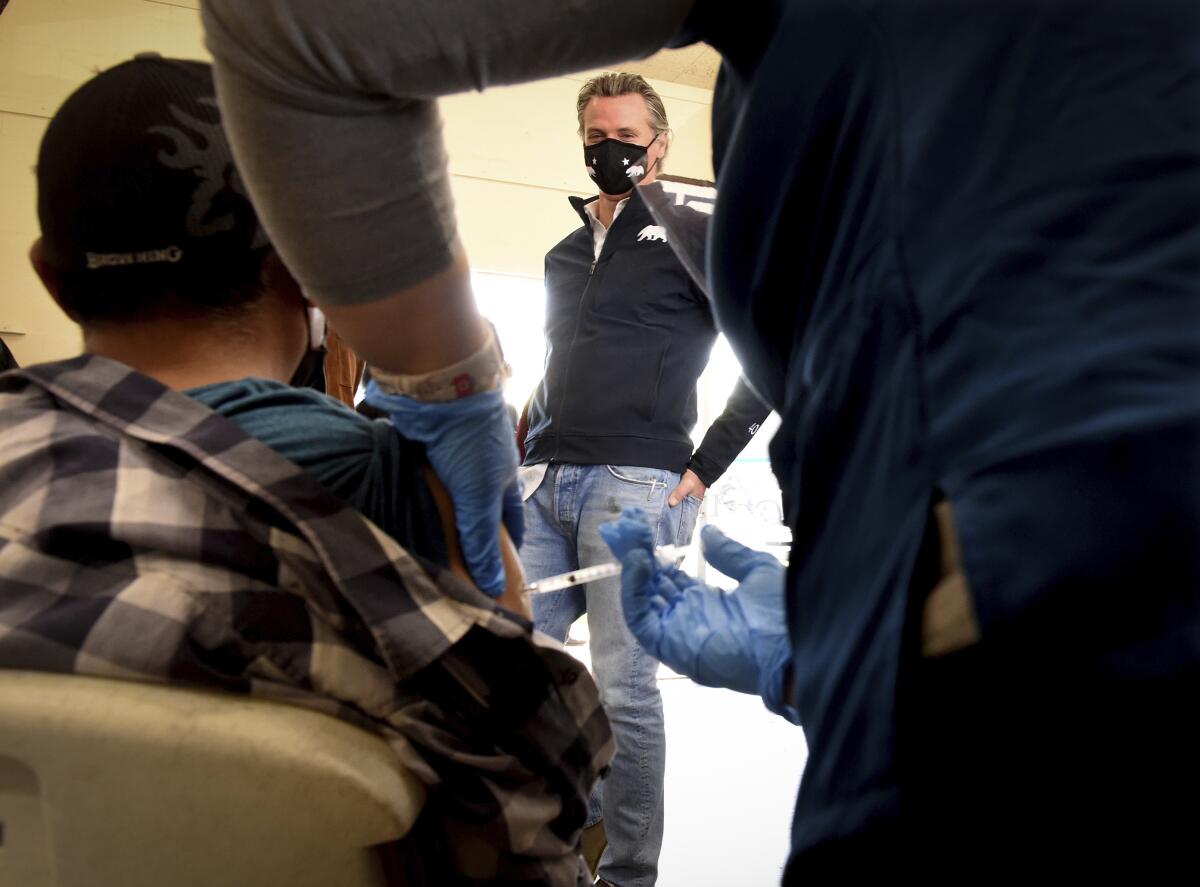 Gov. Gavin Newsom watches a farmworker receive  COVID-19 vaccine