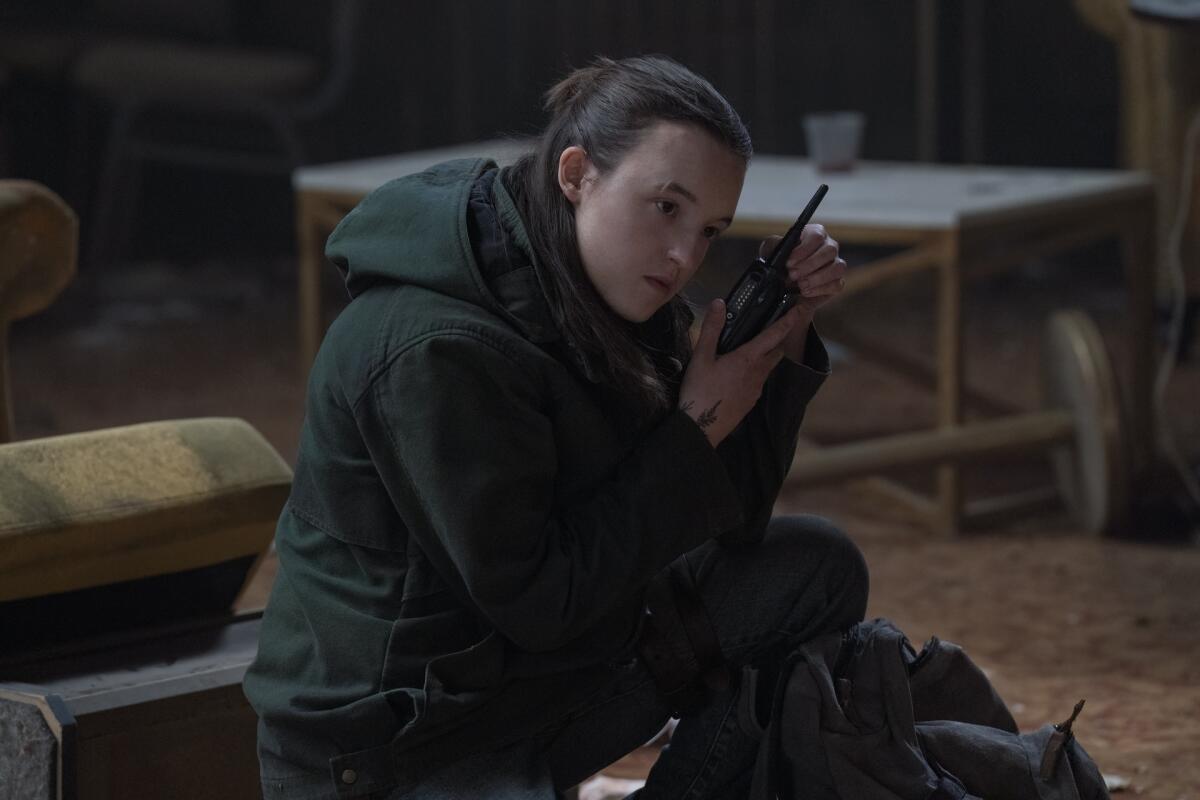 Bella Ramsey holding a walkie talkie up to their ear