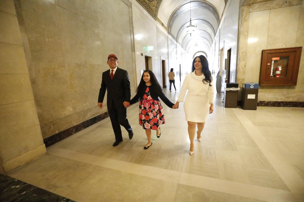 Two adults and a child walk down a hallway holding hands.