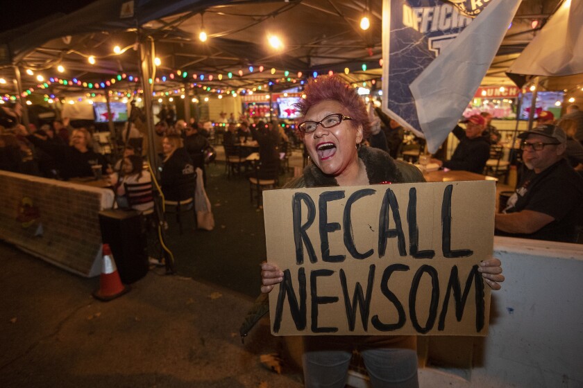 A woman yells outside a bar patio with a cardboard sign that says Recall Newsom