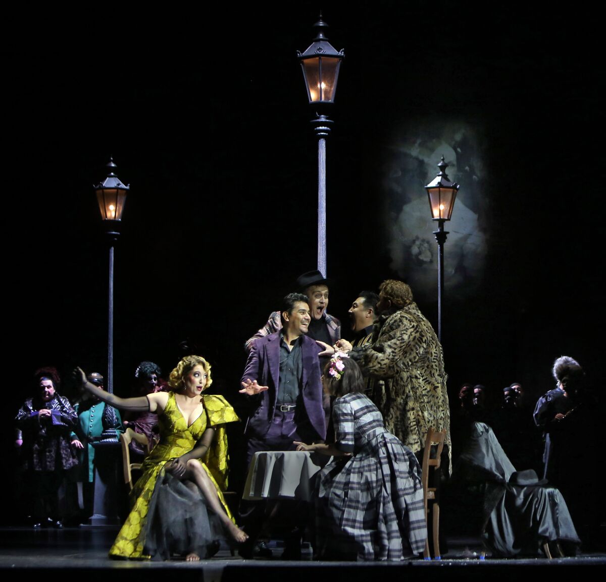 Erica Petrocelli is Musetta (seated left), Saimir Pirgu is Rodolfo (standing center with hand out) and Marina Costa-Jackson is Mimi (seated in plaid dress) in L.A. Opera's "La Bohéme" at the Dorothy Chandler Pavilion.
