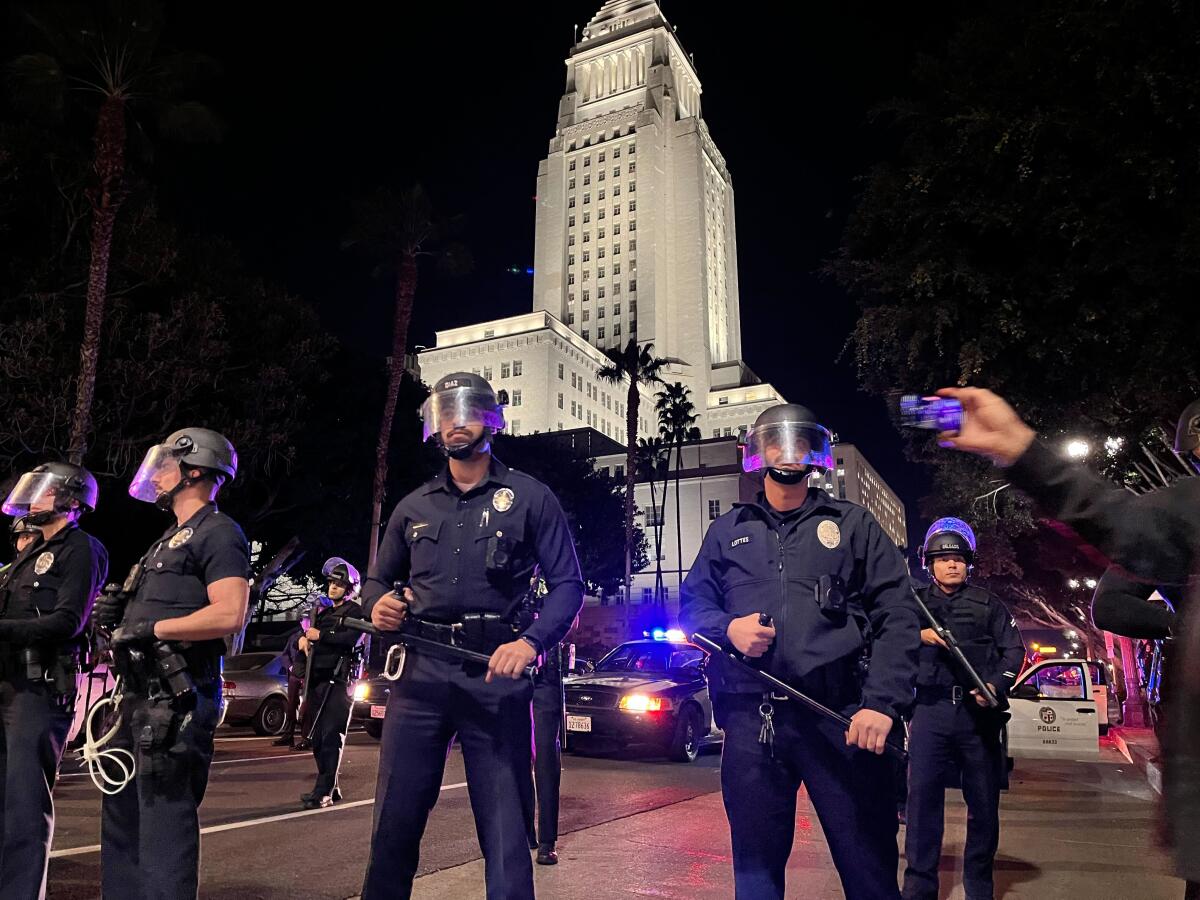LAPD officers stand outside department headquarters as a crowd blocks Main and 1st streets in downtown Los Angeles