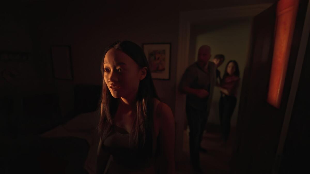 A young woman stares toward a glowing light as three people stand behind her in a dark room's doorway.