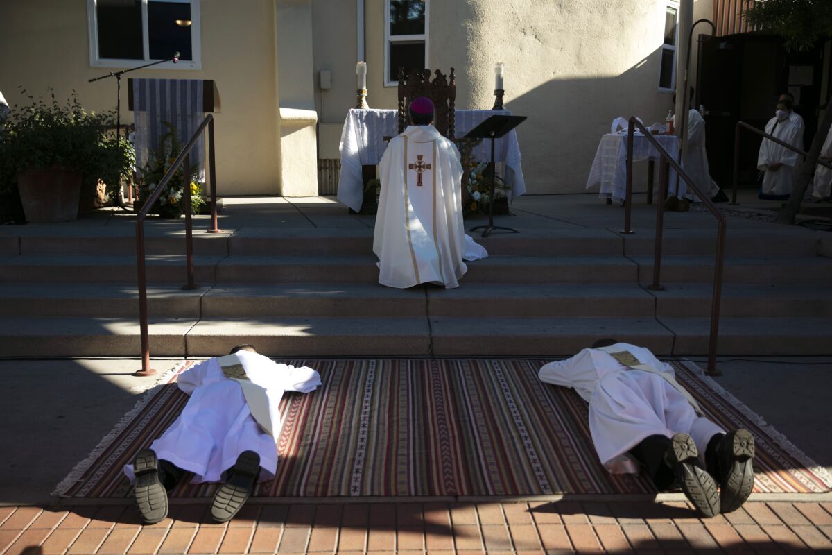 Justin Claravall, bottom left, Gregory Celio lie on a carpet while Bishop Alex Aclan leads a prayer during an ordination ceremony for the new priests at Dolores Mission Church in Los Angeles, Wednesday, July 15, 2020. The ceremony took place outdoors since indoor religious activities have been suspended due to the coronavirus pandemic. (AP Photo/Jae C. Hong)