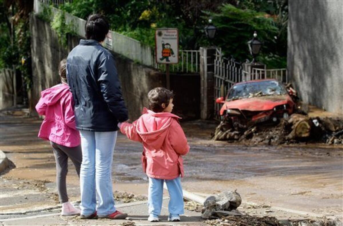 A woman and two children look at a wrecked car outside a school Sunday, Feb. 21 2010, by a road where several cars were carried by floodwaters onto hillside houses on Saturday outside Funchal, the Madeira Island's capital. Rescue workers dug frantically Sunday to free cars and homes buried under heaps of caked mud in Madeira, after torrential flash floods and mudslides killed people on the popular Portuguese island. (AP Photo/Armando Franca)