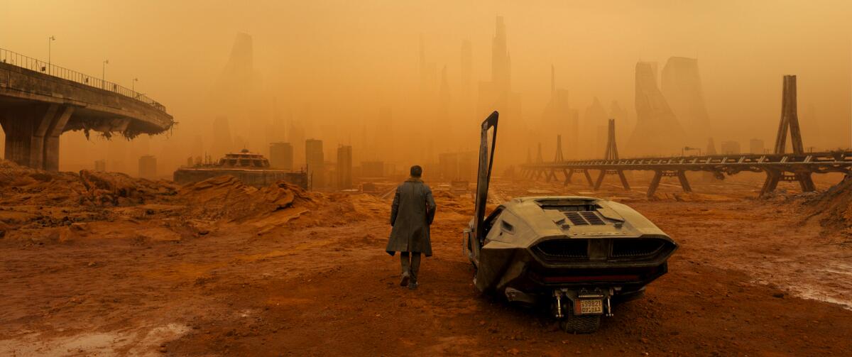 Ryan Gosling walking in a trench coat through an orange, smoggy, desolate cityscape with a futuristic car in the foreground