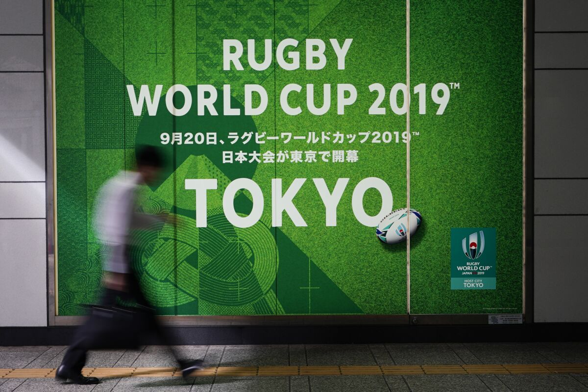 A man walks past a sign promoting the Rugby World Cup Thursday, Oct. 10, 2019, in Tokyo. The powerful typhoon that has caused the first cancellation of the Rugby World Cup games has ended Italy's prospects of reaching the quarterfinals and could upset Scotland's chances of progressing to the knockout stages as well. (AP Photo/Jae C. Hong)
