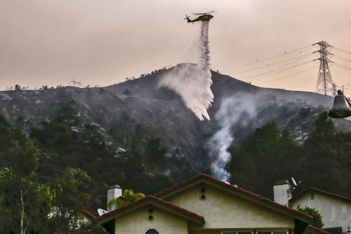 An LA County firefighting helicopter makes a water drop above Westvale Road as Fish fire burns in Duarte on Tuesday morning.