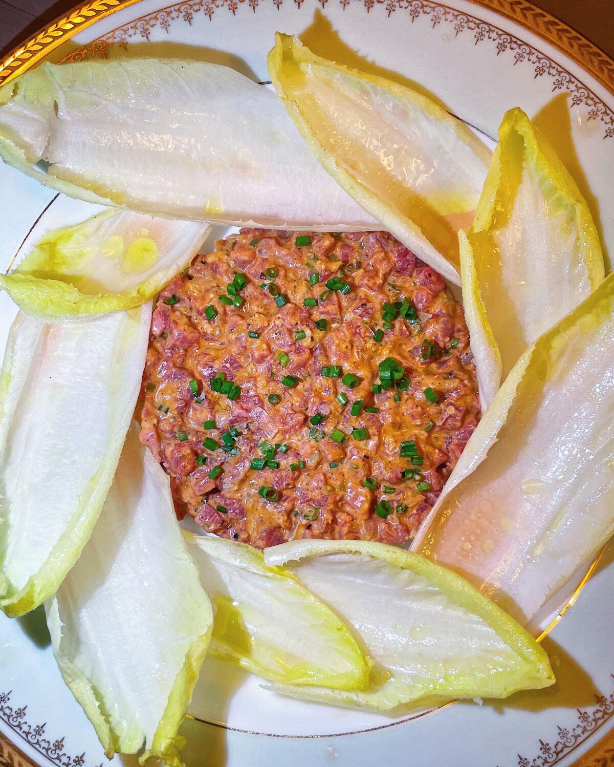 An overhead photo of a circle of chive-topped steak tartare surrounded by endive leaves from Studio City's Cosette Wine Bar