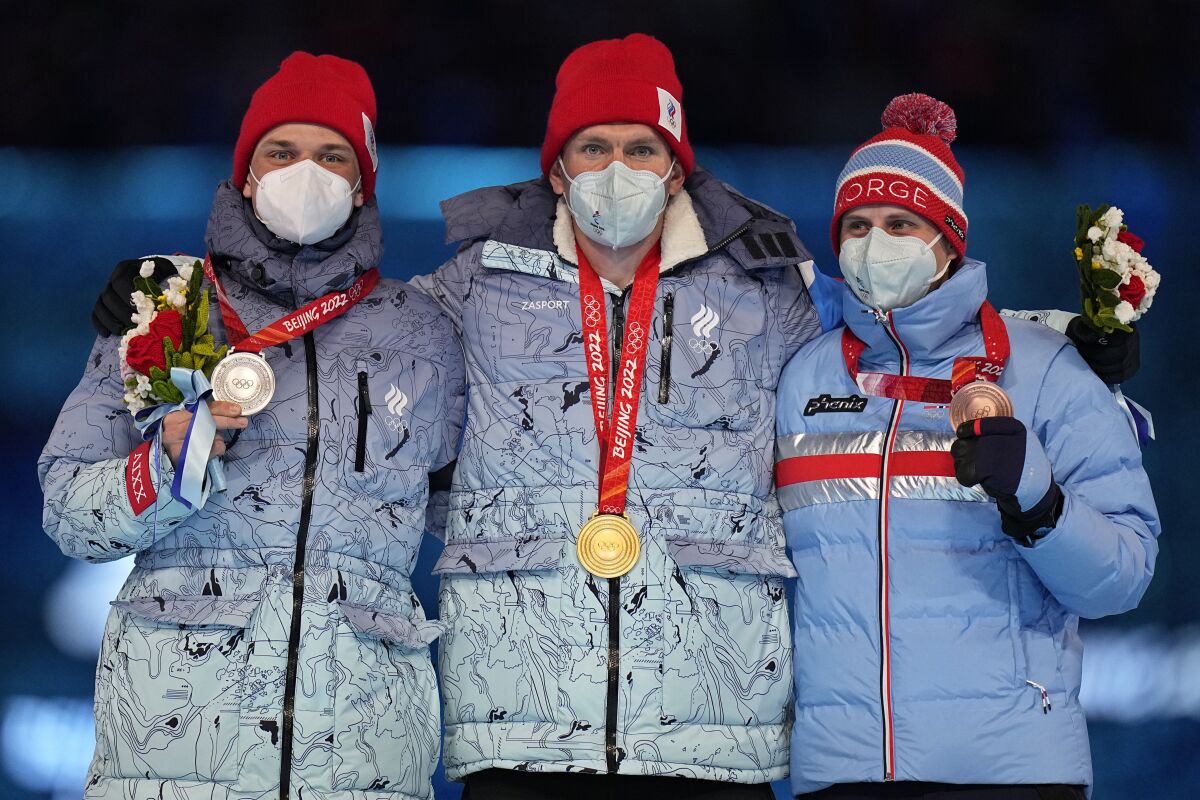 Three men in winter gear and masks stand arm in arm wearing Olympic medals around their necks 