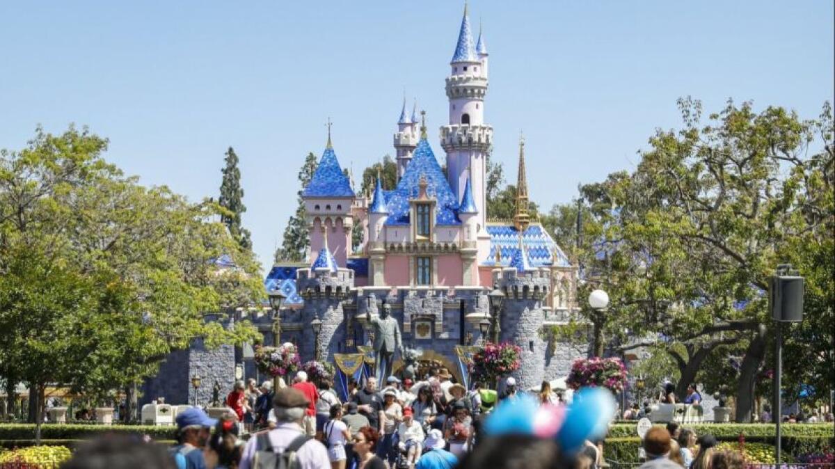 A crowd of people in front of Sleeping Beauty's Castle at a Disney park.