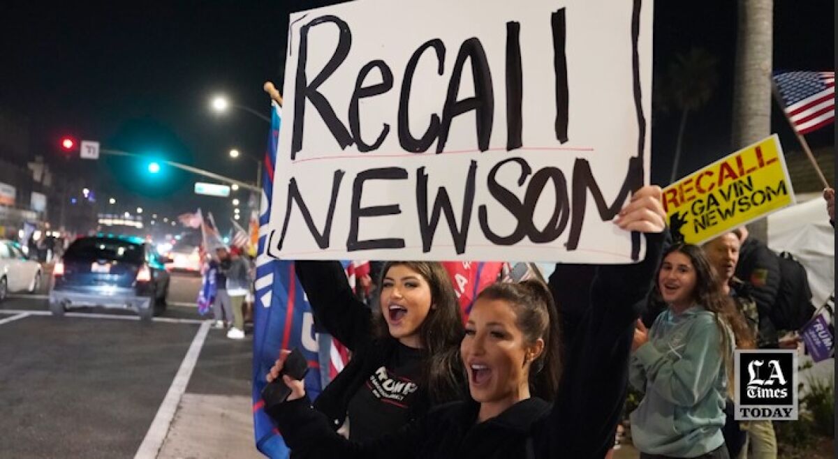 People on a sidewalk hold up a "Recall Newsom" sign