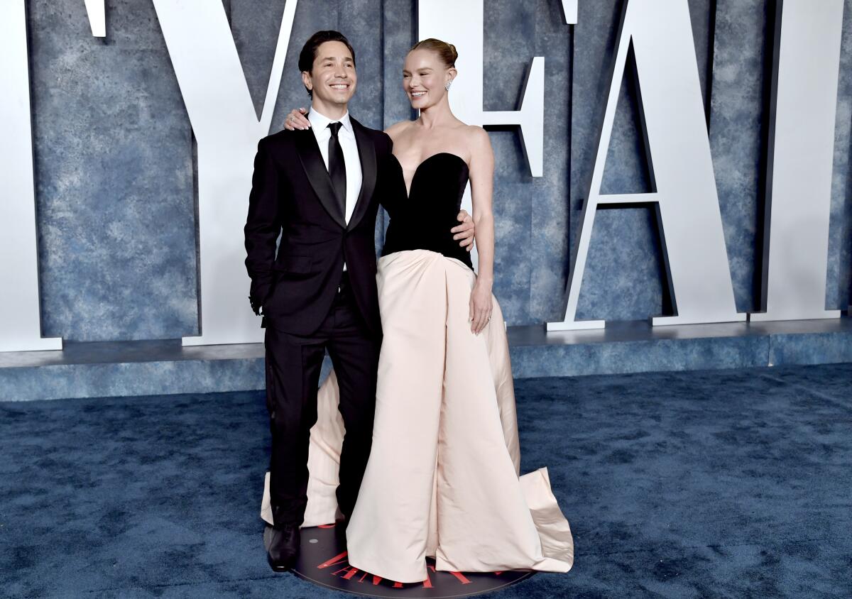 Justin Long, left, and Kate Bosworth pose in formalwear on a blue carpet