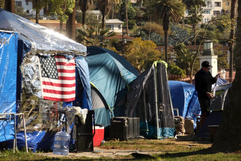 LOS ANGELES, CA - FEBRUARY 27, 2021 - - Against a backdrop of homes Gregory Audette, 52, tidies up his space where he and others live homeless in Echo Park on February 27, 2021. Audette, who is out of work, said he hasn't been living in the park long. Homeless encampments have been proliferating in Echo Park for the past year have become the focus of an increasingly bitter debate between residents, advocates for homeless rights and public officials. The camp, now covering about a third of the park, has evolved into something of a commune with showers, food distribution and governance. (Genaro Molina / Los Angeles Times)