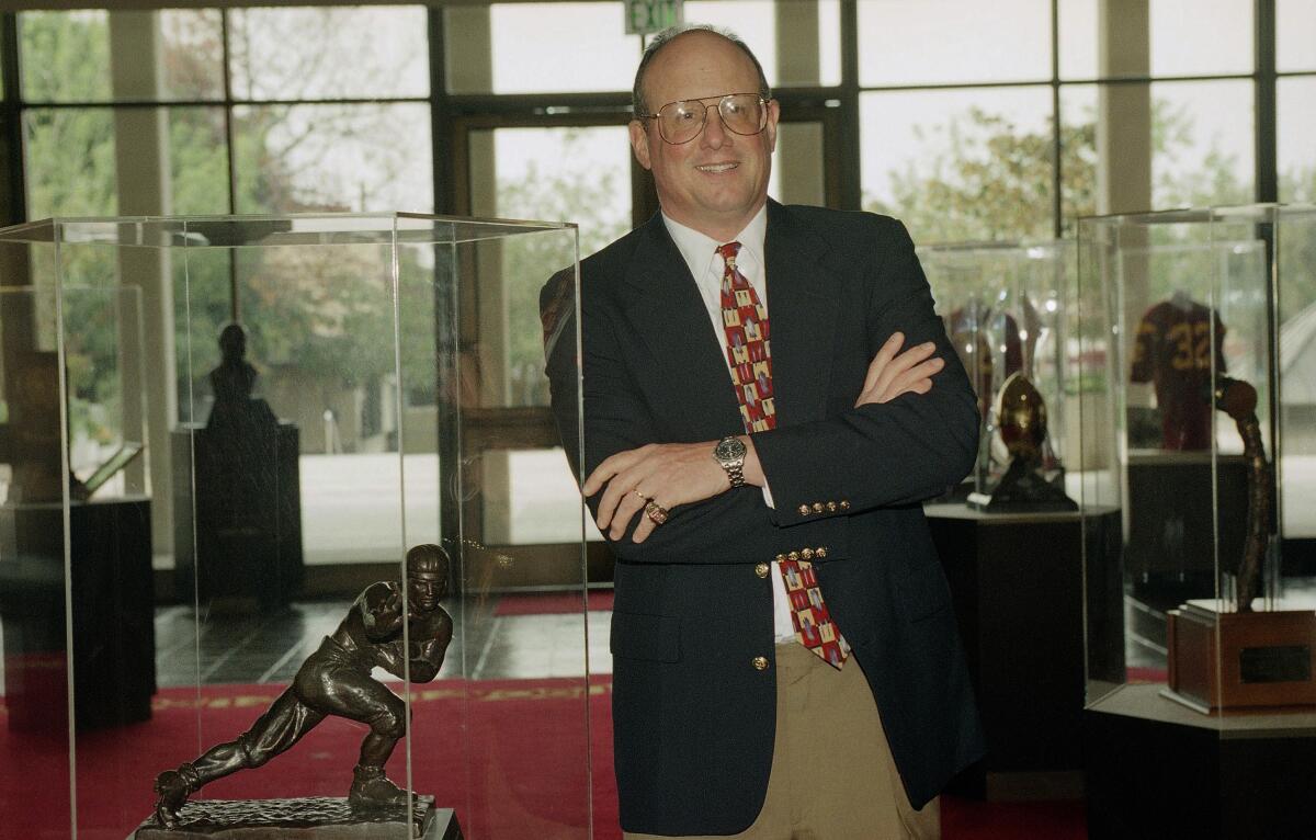 USC coach Paul Hackett poses beside Marcus Allen's Heisman Trophy on the USC campus.