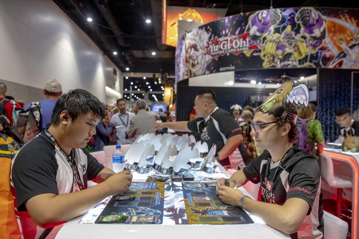 Two men sit at opposite sides of a table playing a card game.