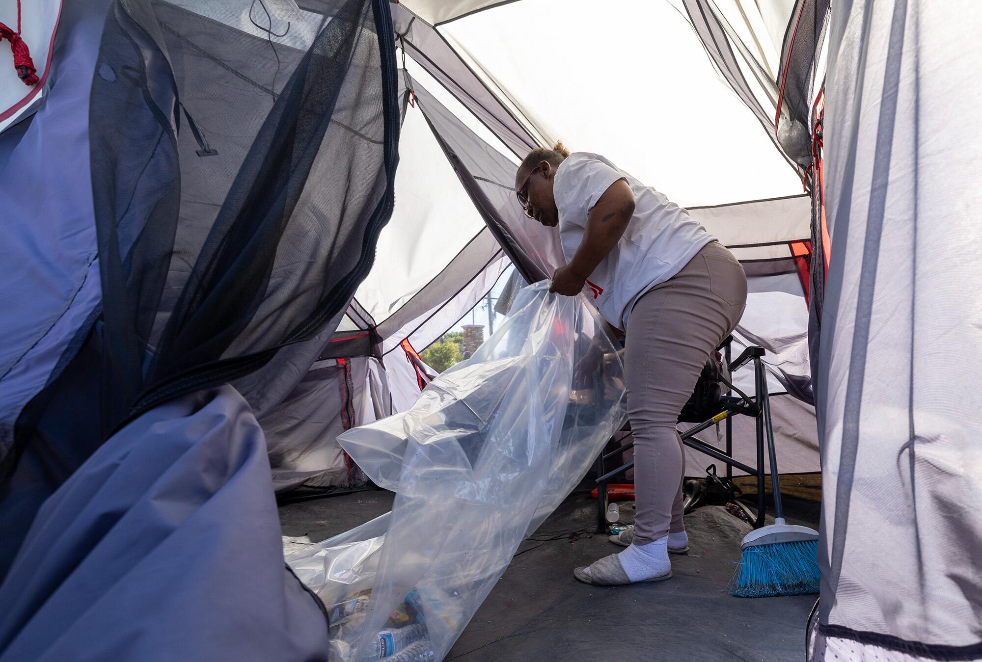 A woman in a tent puts items into a plastic bag.