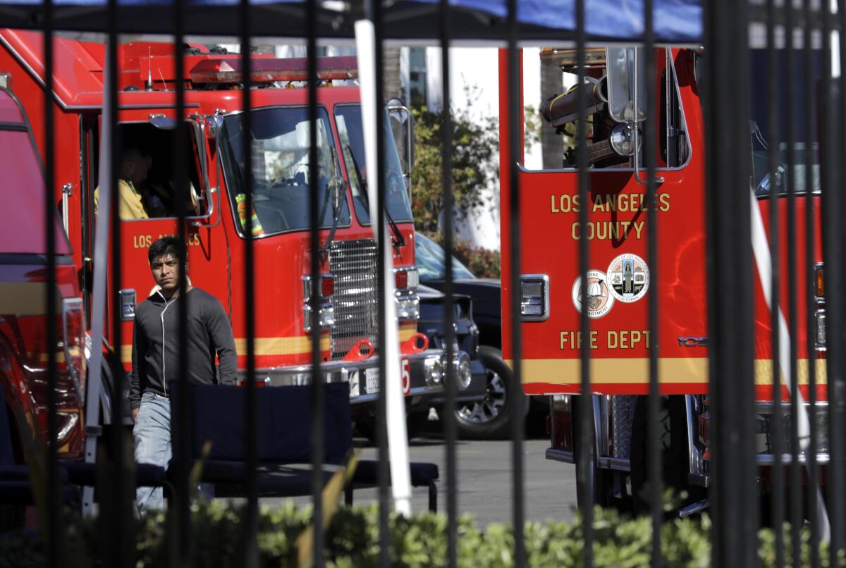 A man walks past fire trucks in the parking lot of the Plaskolite factory in Compton