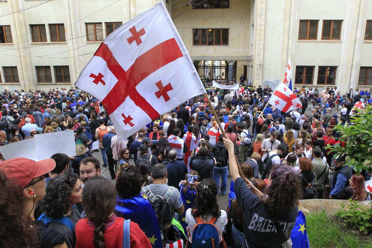 Demonstrators wave Georgian national flags outside a building.