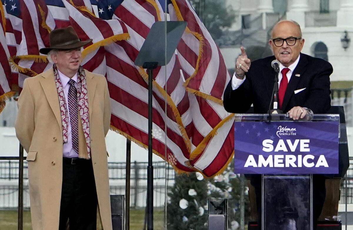 John Eastman stands with Rudolph W. Giuliani, who speaks at a lectern reading "Save America."