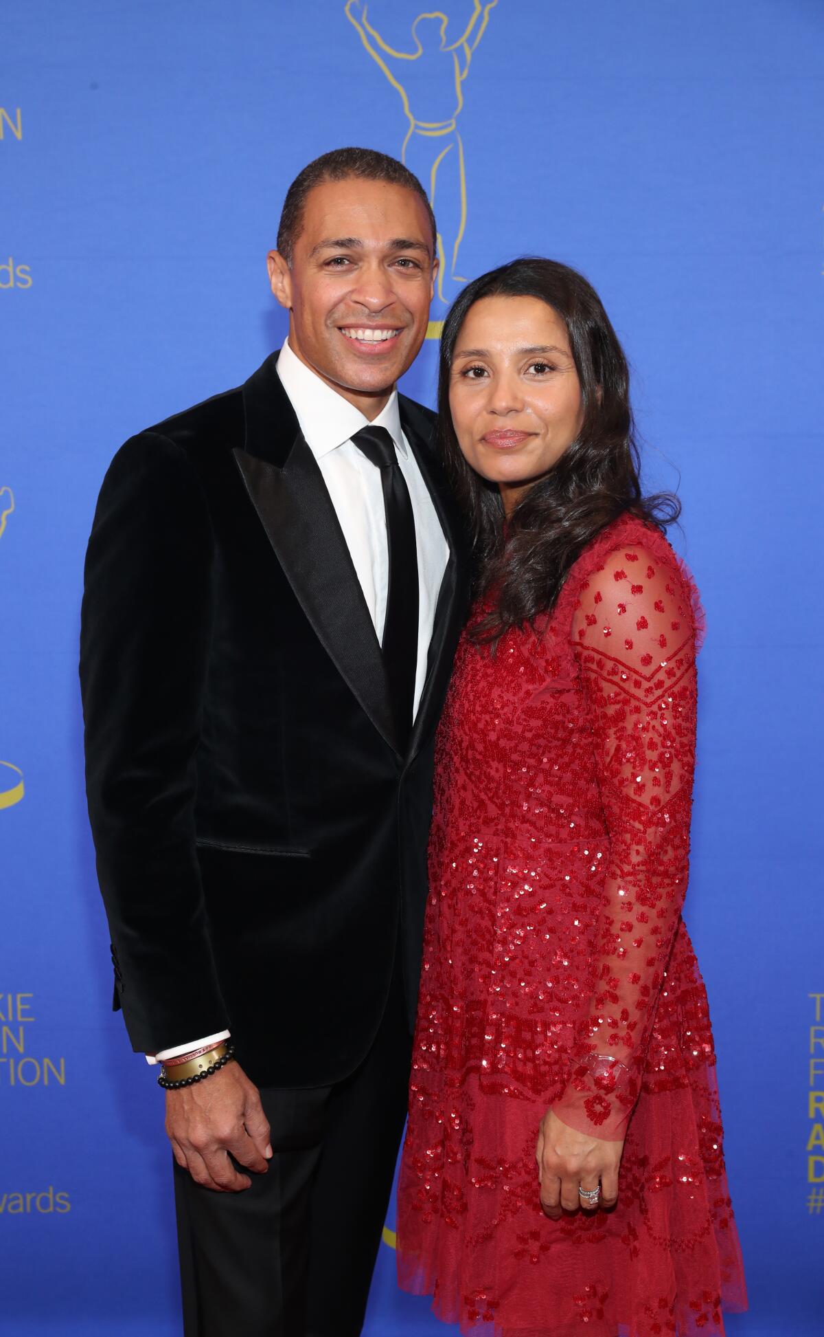 A man in a black suit and a woman in a red dress stand close together.