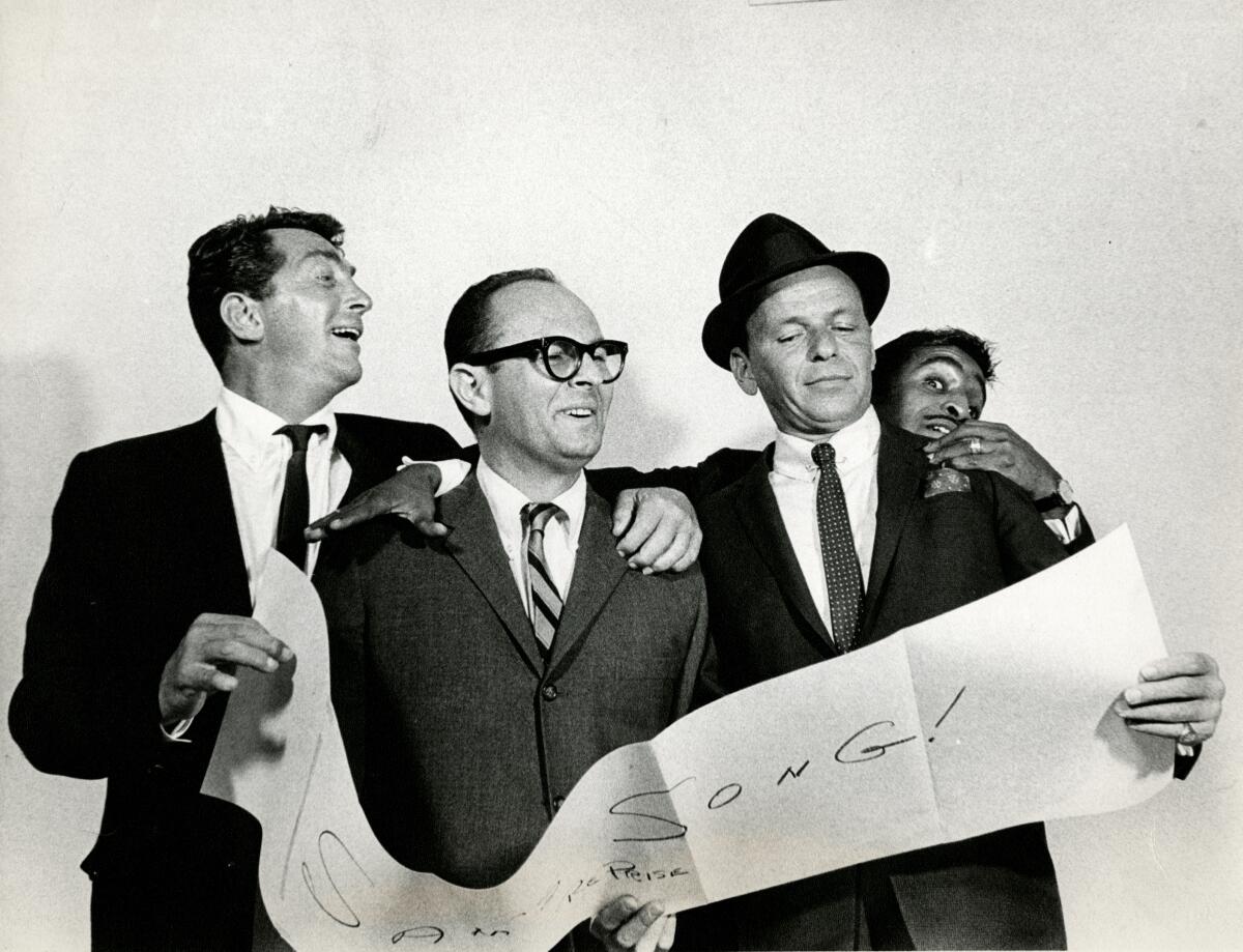 A black-and-white photo of four men in suits holding a paper banner.